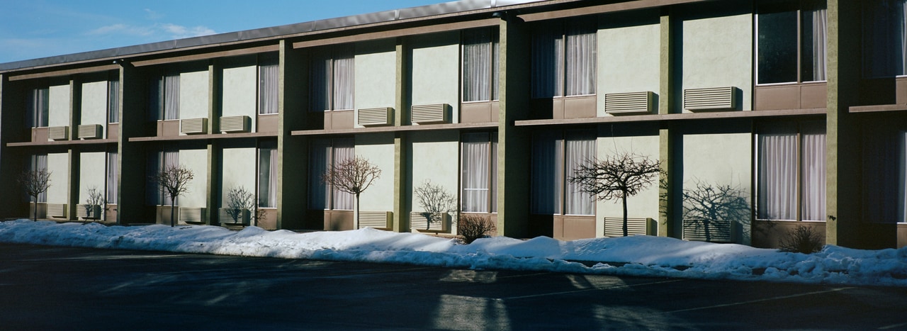 Bare trees casting shadows across a motel facade above a strip of snow