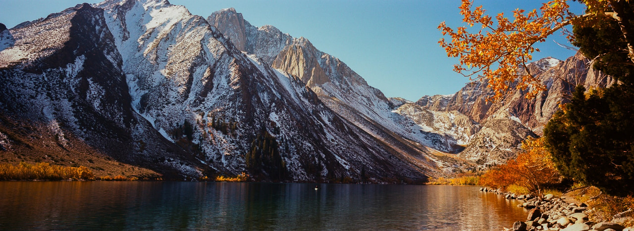 A snow-covered peak reflected across the lake beside autumn foliage