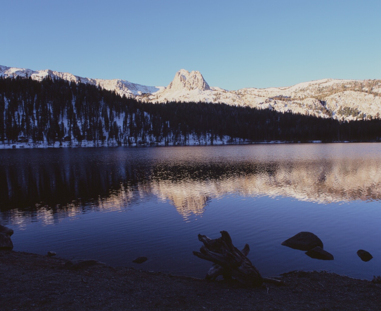 Rocks at the edge of a blue lake reflecting a snowy ridge