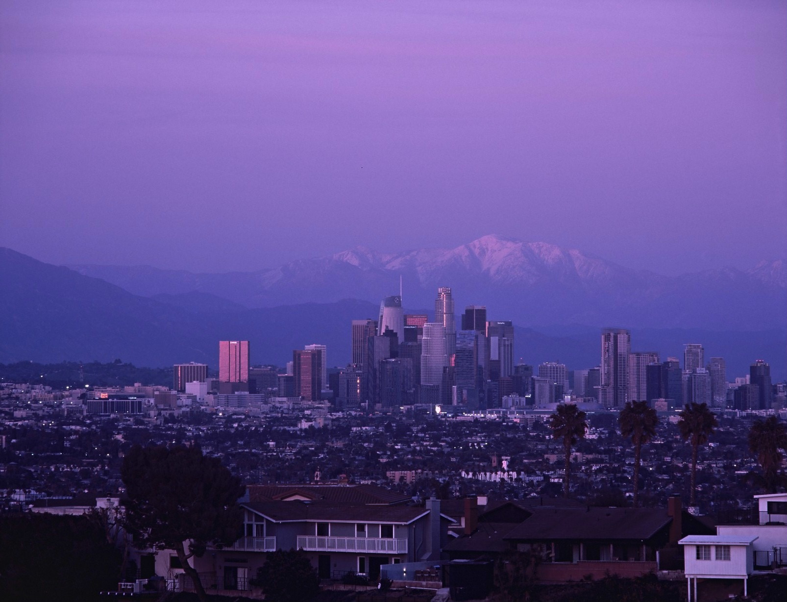 The Los Angeles skyline beneath a violet sky and distant snowy mountains