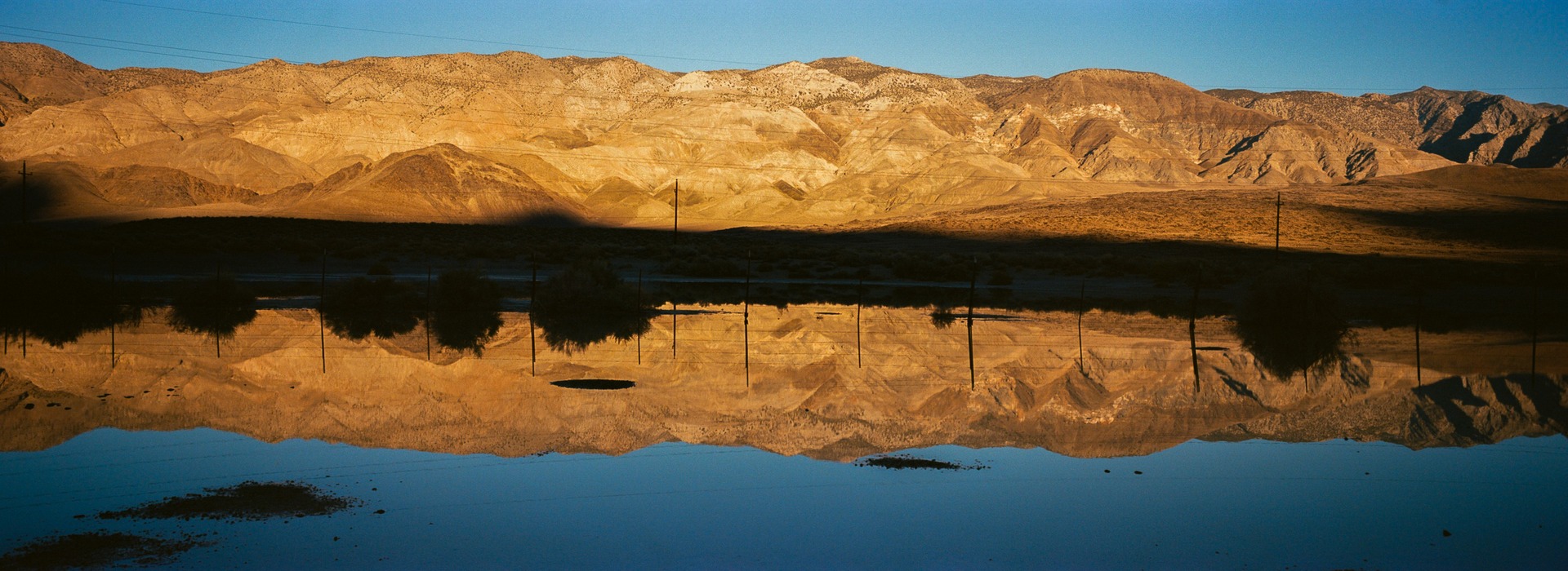 Golden mountains and utility poles reflected across a dark shoreline