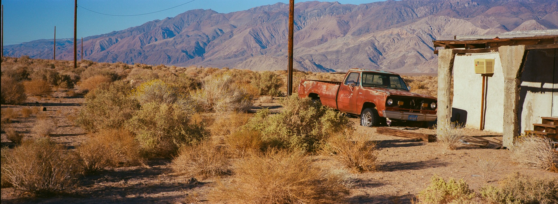A red pickup and a weathered building among desert scrub