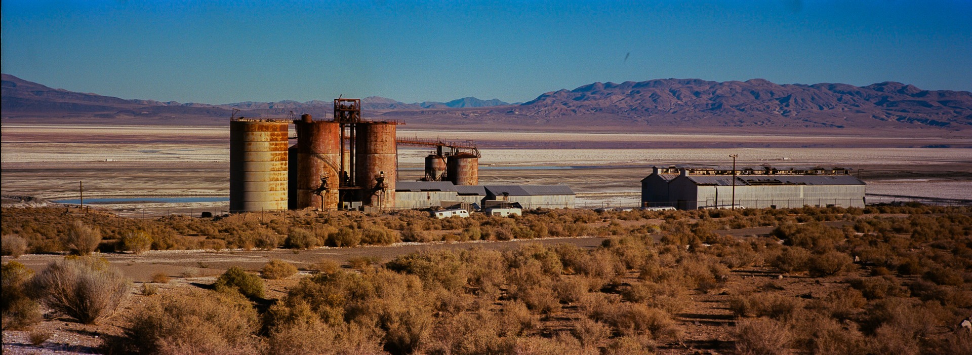 Rusted industrial silos overlooking a pale dry lake bed
