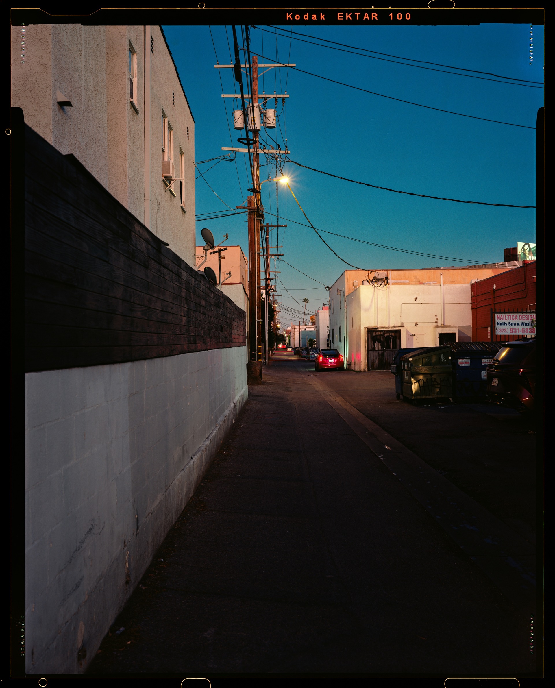 Warm light on a narrow urban alley beneath wires and blue sky