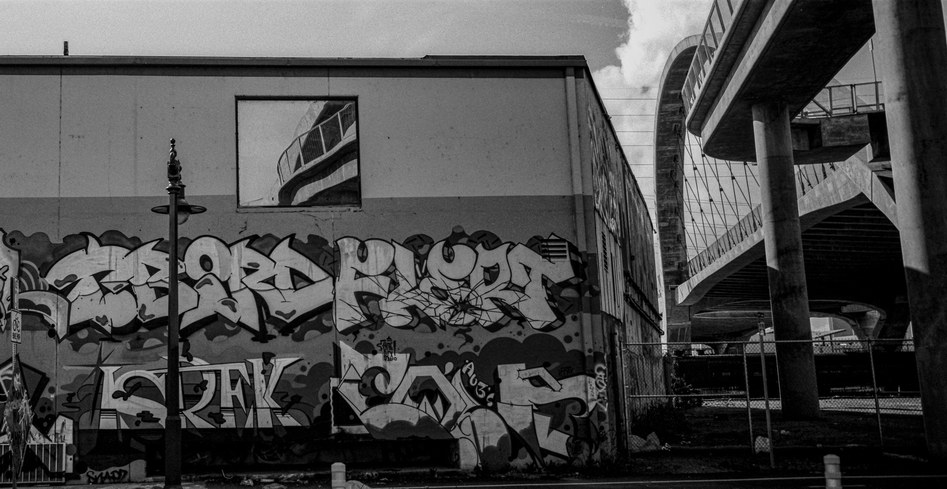 Black-and-white photograph of graffiti and a spiral ramp beside a bridge