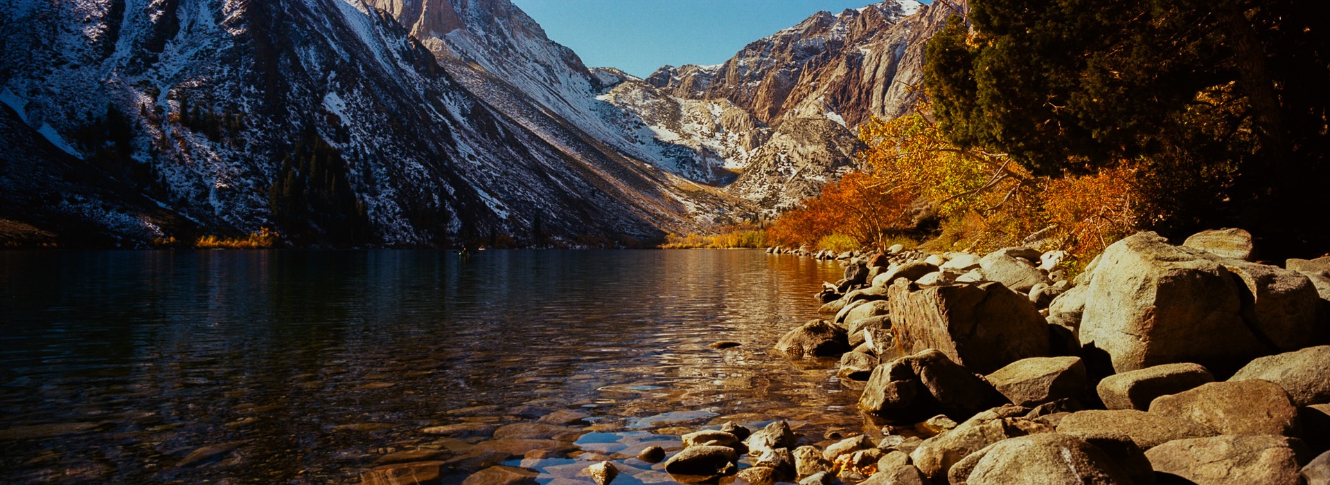 Clear lake water and shoreline boulders beneath steep mountains
