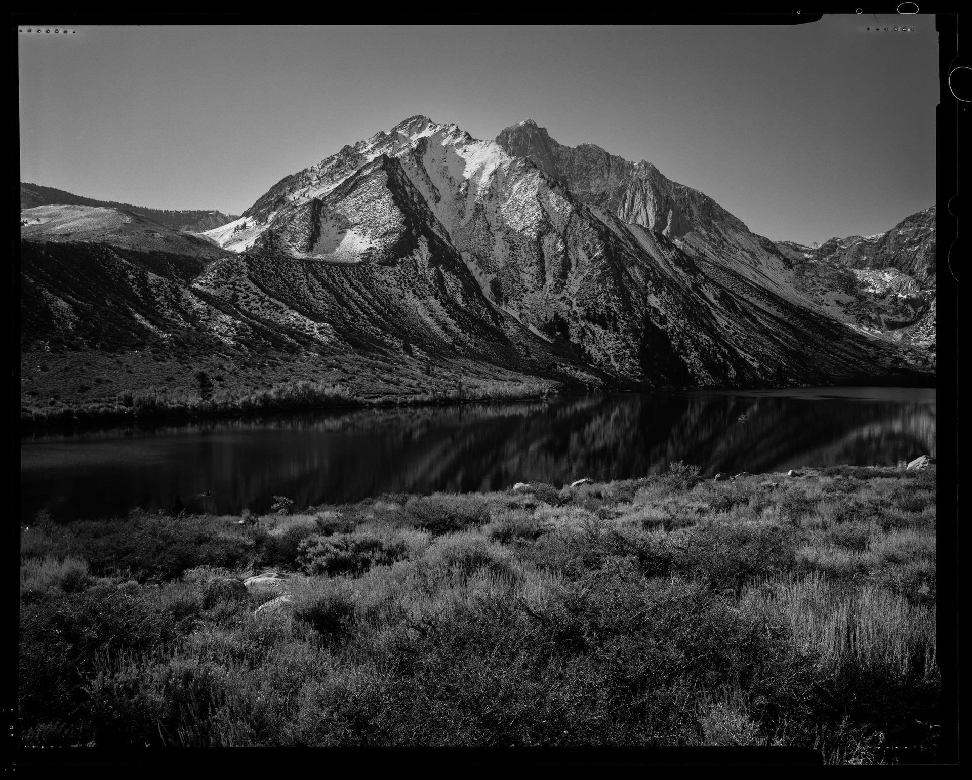 Black-and-white photograph of a snow-dusted mountain reflected in still water